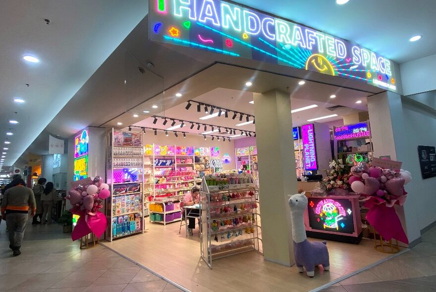 The shopfront of a Japanese-style craft workshop with brightly coloured craft materials on shelves and a neon sign.