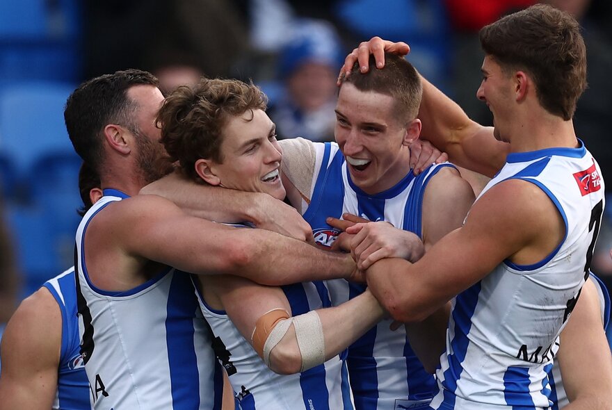 A huddle of North Melbourne AFL players hugging and congratulating each other on the football field.
