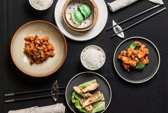 Asian dishes on a black table, including dumplings and rice.