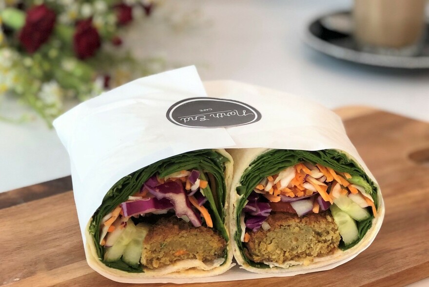 A halved falafel wrap on a wooden board.