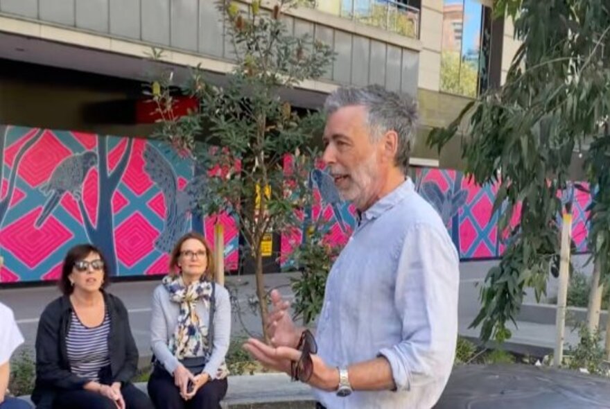 A tour guide presenting to a small group of people sitting down in a public space. 