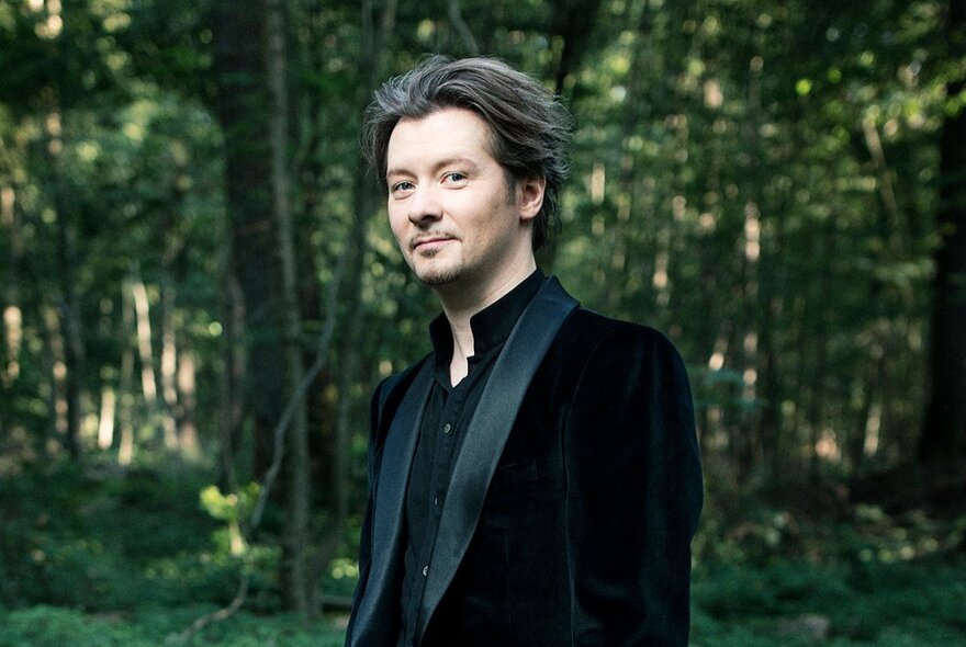 Flugelhorn virtuoso Sergei Nakariakov standing in a forest wearing a suit with black satin lapels. 
