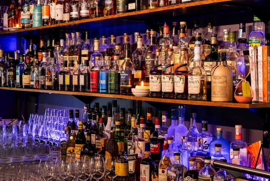 Many bottles of different alcohol and glasses, on shelves behind a bar.