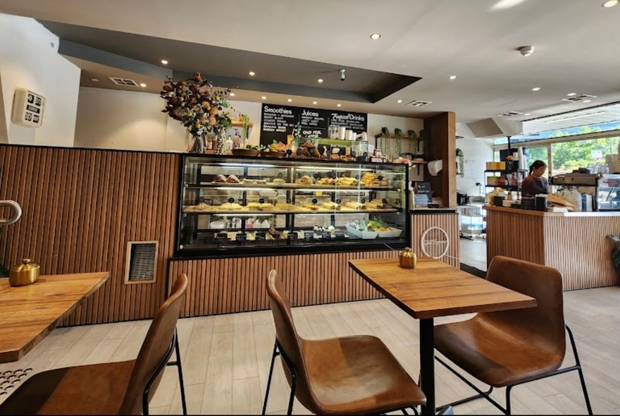 Cafe with wooden chairs and tables, glass serving counter and display cabinet.