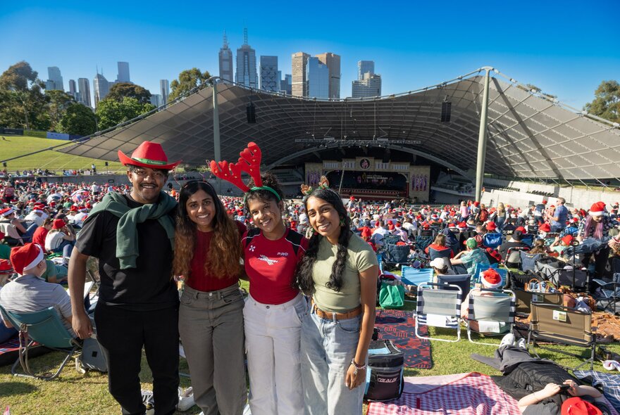 People wearing Christmas novelties, standing in front of crowded Sidney Myer Music Bowl.