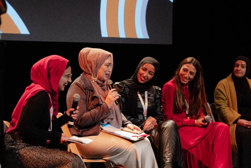 Five muslim women on stage for a panel discussion.