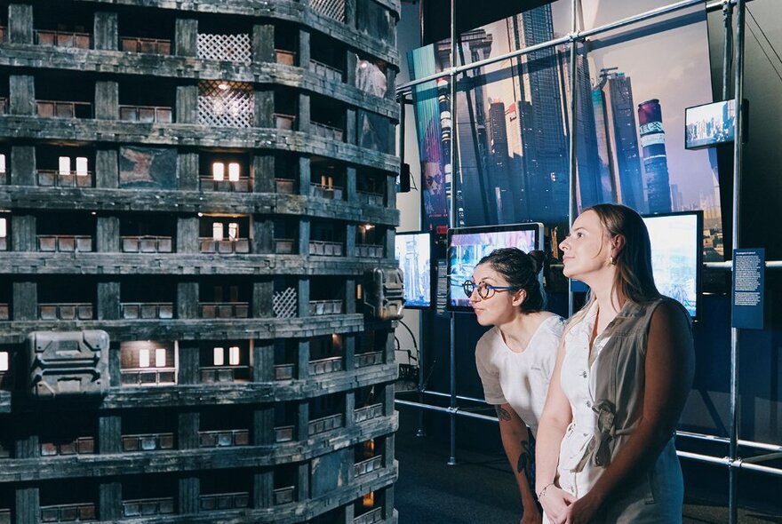 People peering at a model of a dilapidated tower block in a museum exhibition setting.