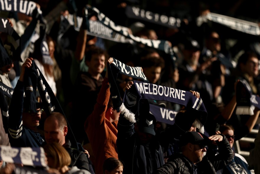 A crowd of Melbourne Victory supports holding up banners in the stands. 