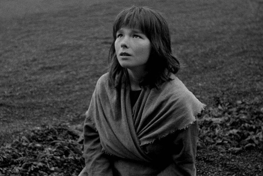 Artist Björk posed in a field wearing a wrap around shawl, black and white image.