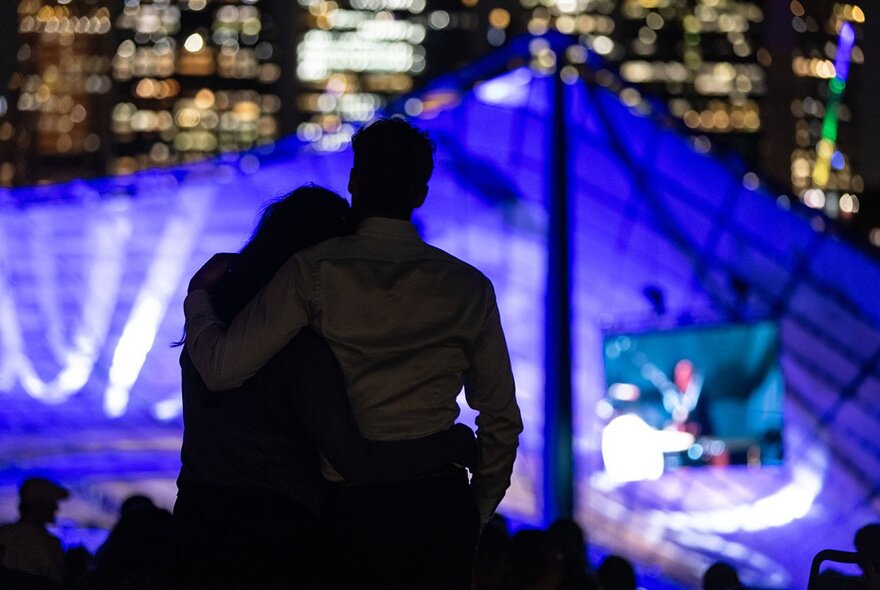 Silhouette of two people leaning into each other watching a concert at Sidney Myer Music Bowl. 