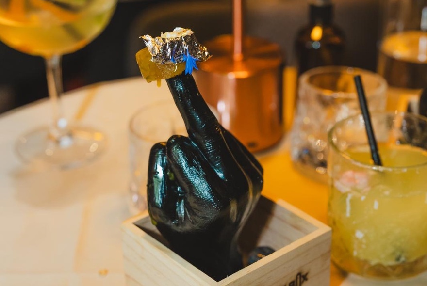 Box containing a hand-shaped creation on a dining table with drinks.