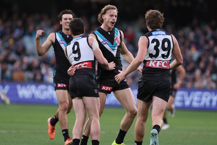 Four Port Adelaide players come together on the football field in celebration.