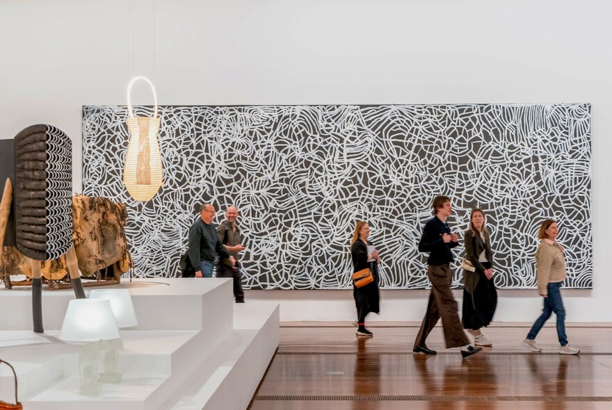 A small group of people walking past a large painting in a gallery, being led on a guided tour.