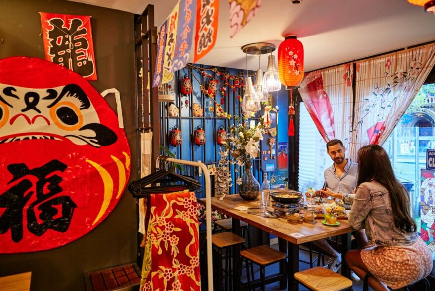 Interior of a restaurant, with people seated and dining at a high table at the window, Japanese artwork and decorations adorning the walls. 