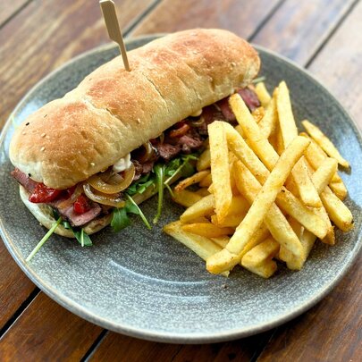 A bread roll with steak and salad inside, with chips.