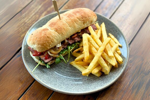 A bread roll with steak and salad inside, with chips.