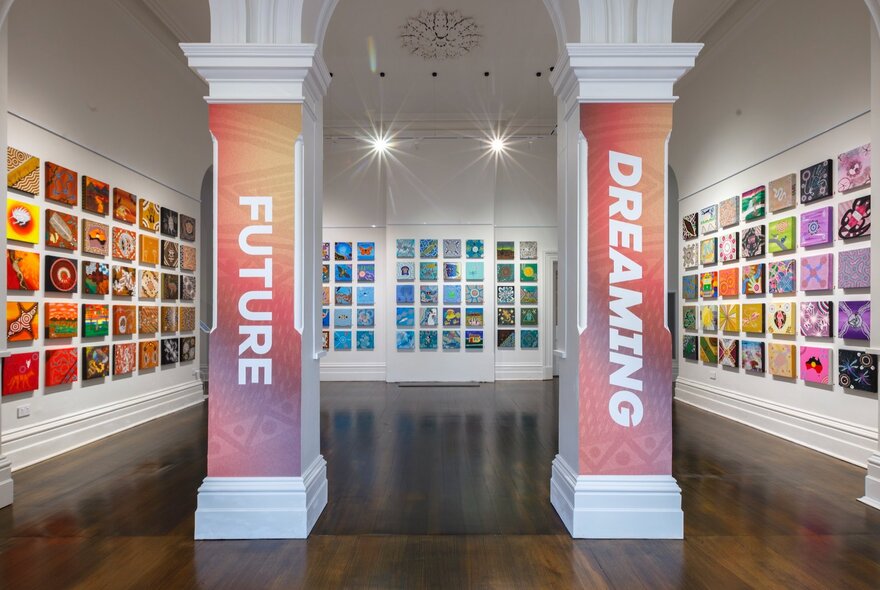 An installation view of many artworks displayed on three walls in a gallery space, with the title of the exhibition FUTURE DREAMING, written on two pillars at the entrance to the exhibition space.