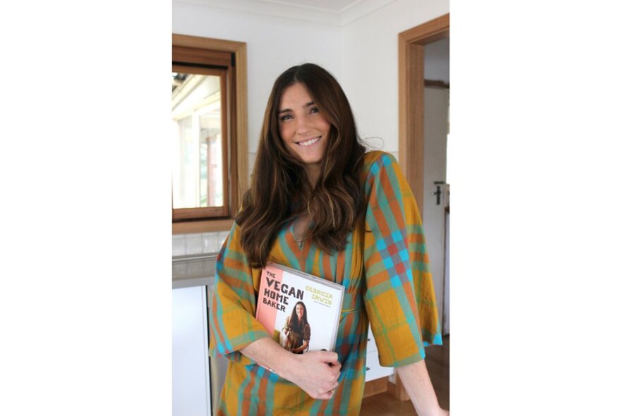 Cookbook author Georgia Irwin standing inside a room in a house holding a copy of her cookbook in front of her.