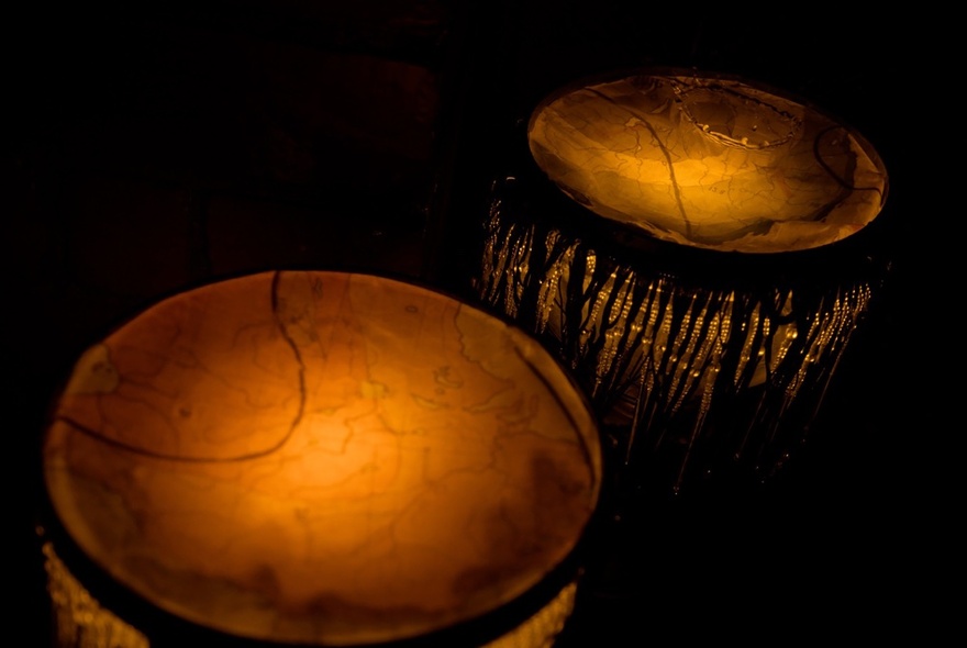 Two outdoor drum instruments in the dark, lit from within, designed to be played by the rain and wind.