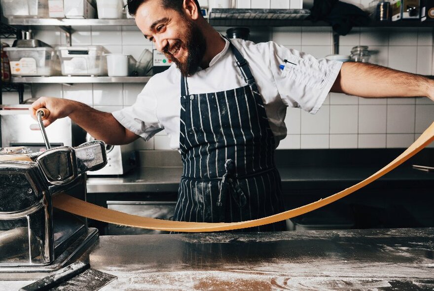 A chef making a long sheet of pasta using a pasta machine.