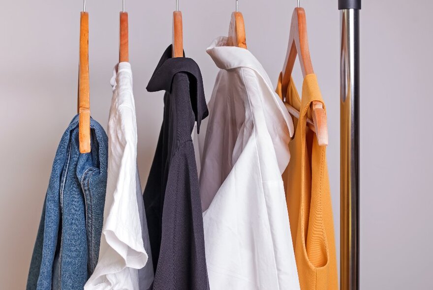 Clothes hanging on five wooden hangers on a clothing rack.