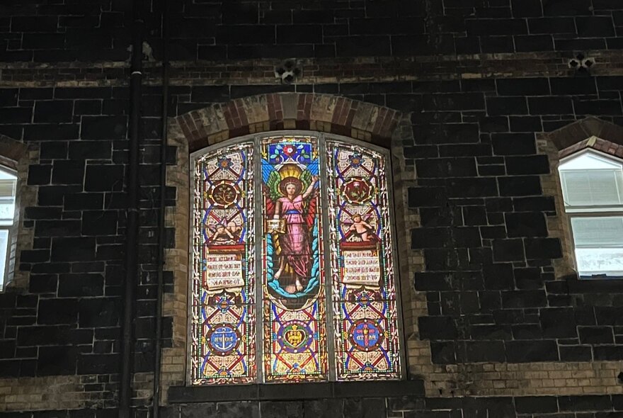 An ornate stained glass window in a bluestone building