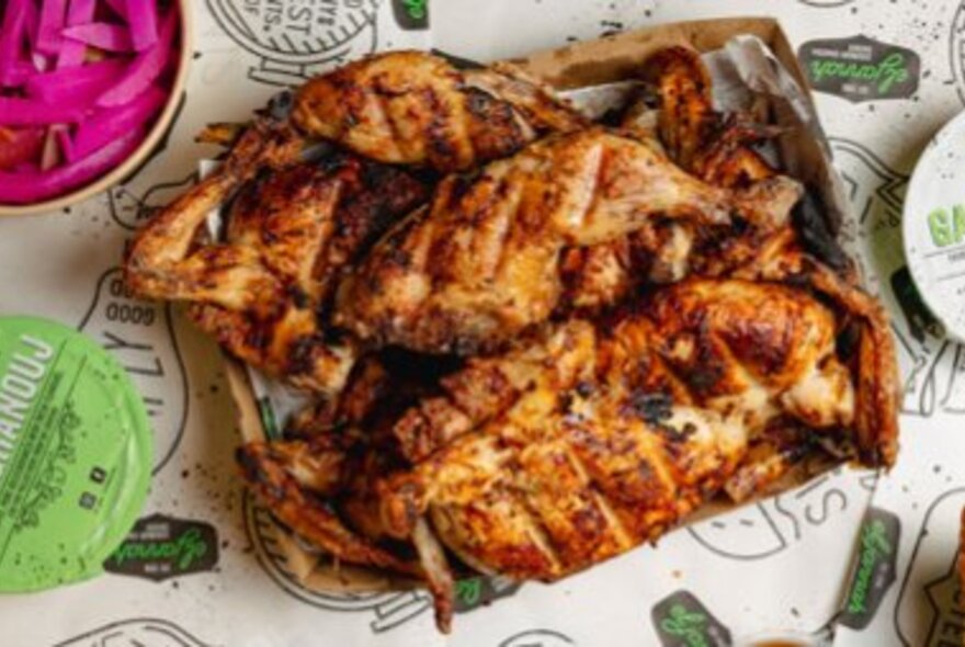 Box of charcoal chicken on a table with dips.