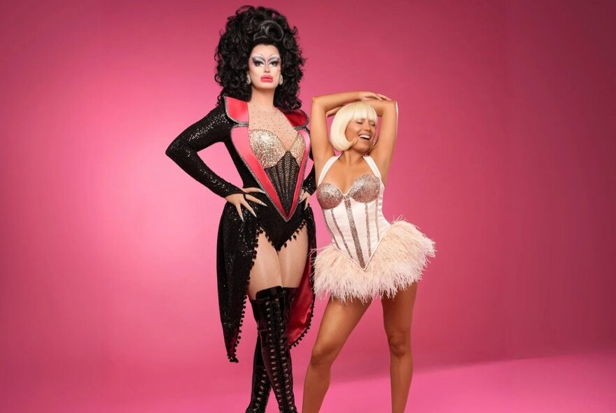 Two burlesque performers in costume, posed against a pink background.