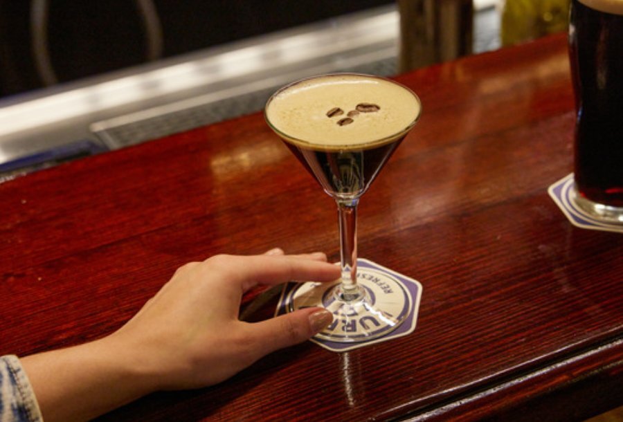 A woman's hand holding an espresso martini on a wooden bar.