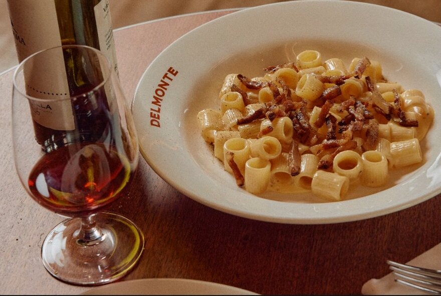 Bowl of pasta and glass of red wine on a wooden table.