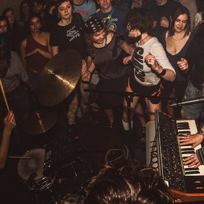 An intimate live music performance with a keyboard player and a drummer playing to an enthusiastic crowd in a dimly lit venue.