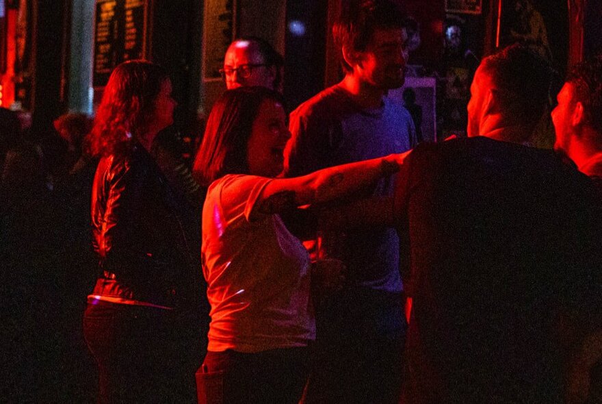 People dancing in a darkened bar, lit up by a red light.
