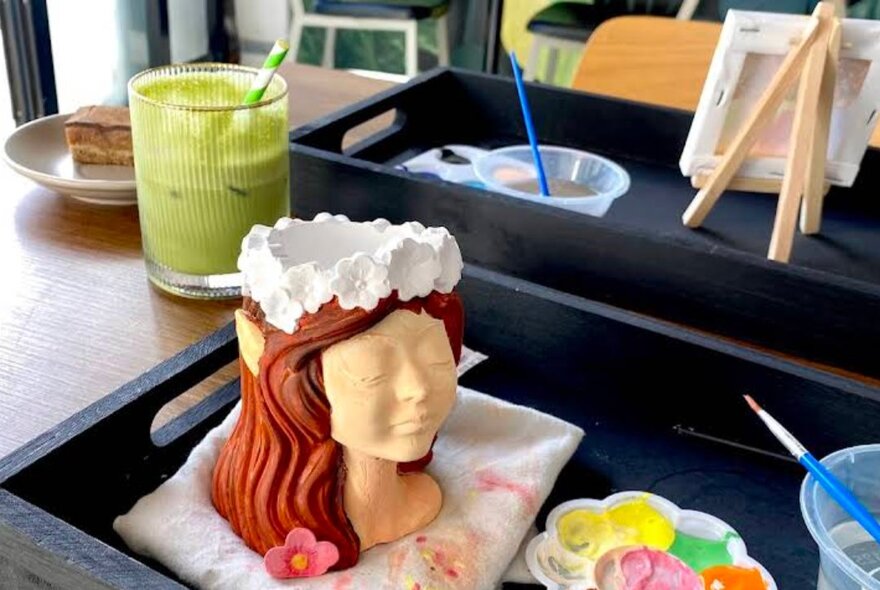 Matcha drink next to a clay sculpture with paints and palette.
