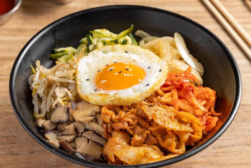 Korean Bibimbap, a stir-fried dish with a fried egg on top served in a black bowl.