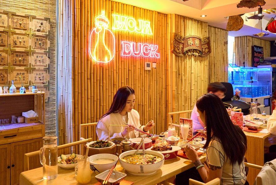 People eating in a Chinese restaurant under a neon duck sign.