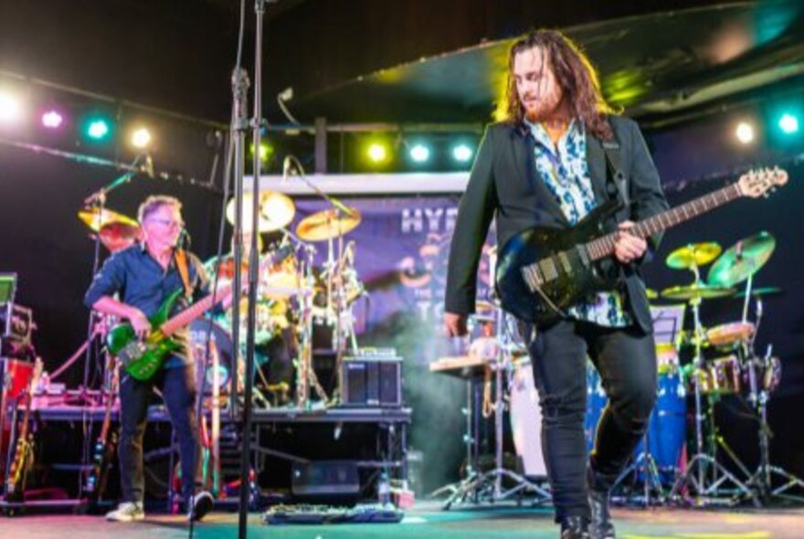 Two guitarists playing their instruments on stage with two drummers behind them.