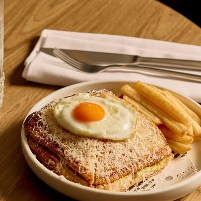 A fried egg resting on top of a toasted jaffle, with a serve of fries, on a plate.