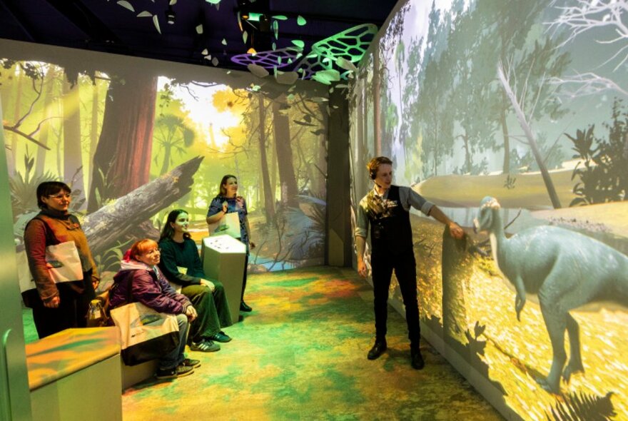 Tour participants listening to a guide as he points at a projection of a dinosaur at the Melbourne Museum.