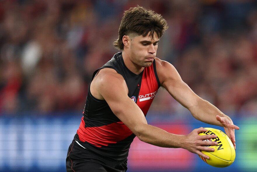 An Essendon AFL football player concentrating as he is about to kick a yellow football during a match.