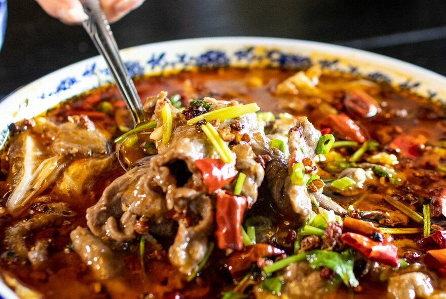 Close up of bowl of spicy stew, chopsticks held over top.