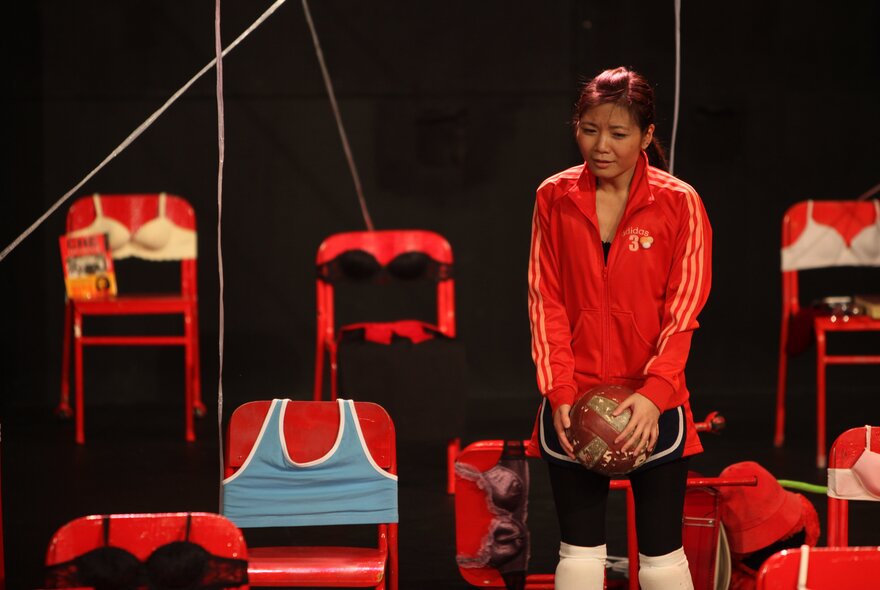 Performer on stage with chairs draped with clothing.