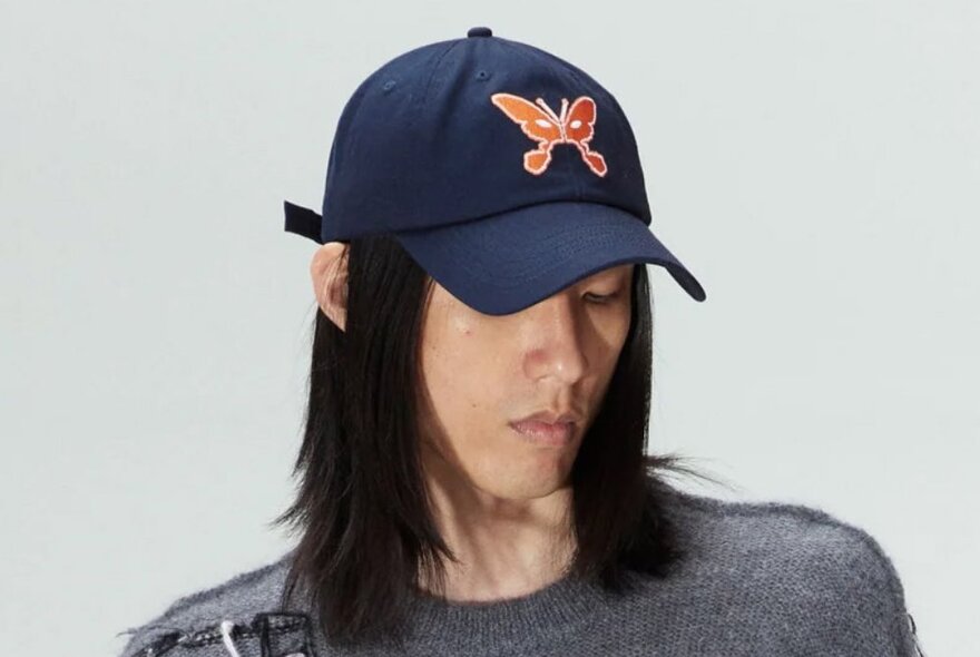 A model wearing a navy hat with an orange butterfly on it. 