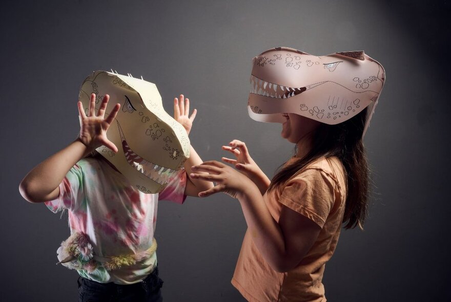 Two people with paper dinosaur hats interacting with their hands out like claws. 