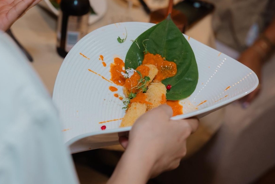 Hand holding orange food on a white plate.
