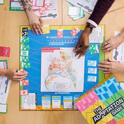 Top down view of hands leaning across a board game on a table and moving the tokens and cards, the group of people are in the act of playing the game.
