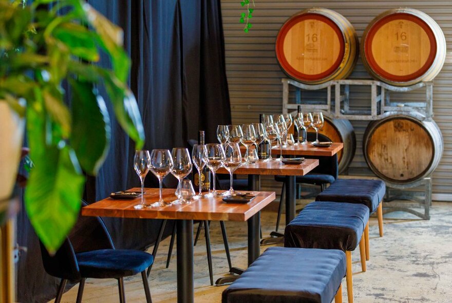 Bar interior with wine barrels and tables with bench seating set with wine glasses.