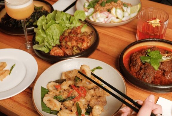 Hands using chopsticks to select food from a plate, from a table filled with plates of food in a restaurant.