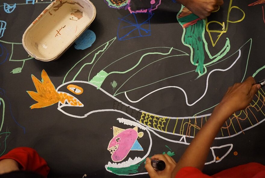 Looking down at children's hands using coloured chalk to create an artwork on a blackboard.