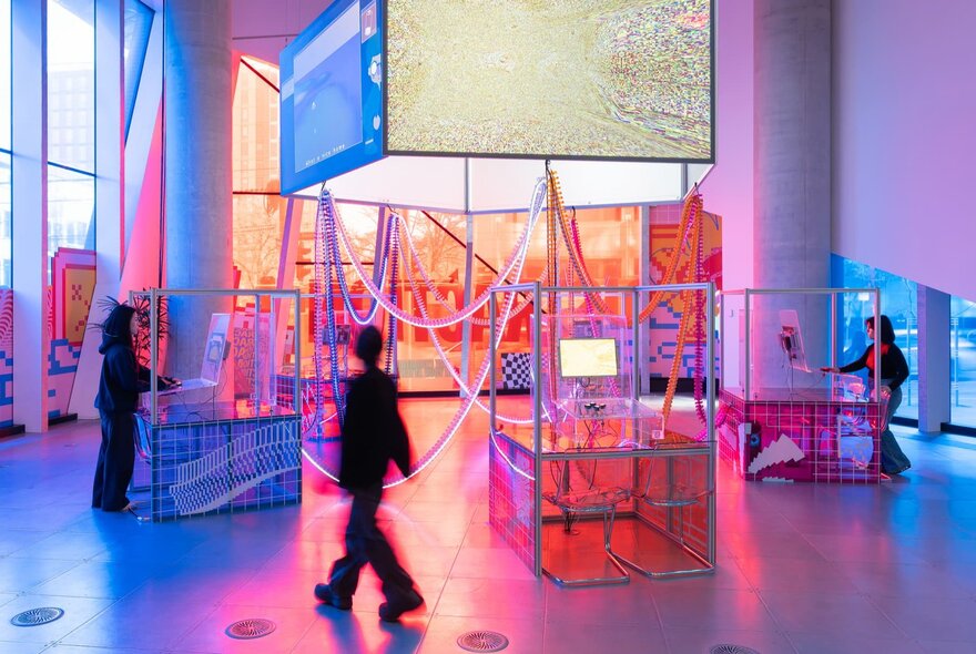 Three people interacting with a neon light installation in a gallery.