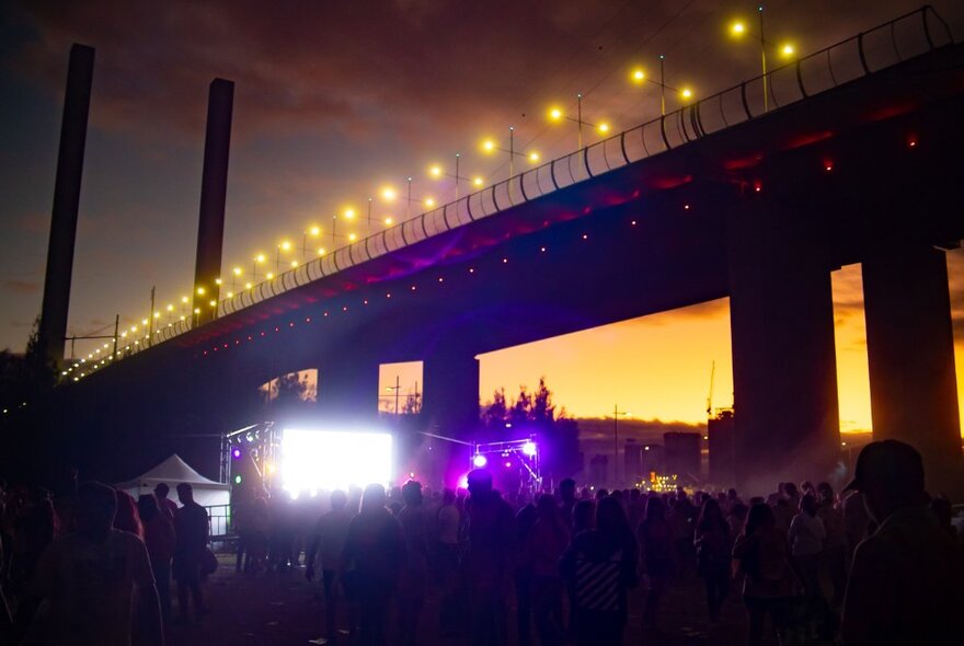 People in the dark underneath the Bolte Bridge looking at an illuminated screen.